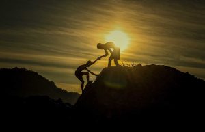 Two people helping each other at the top of the mountain