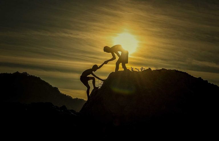 Two people helping each other at the top of the mountain